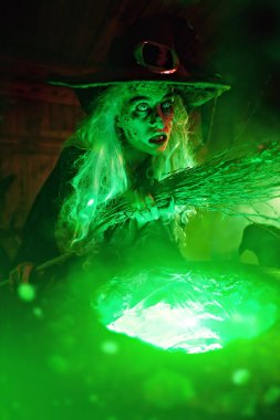 Korkunç cadı süpürgesini sihirli iksirle kazanın yanında büyülüyor. Cadılar Bayramı. Korkunç hikayeler.. 