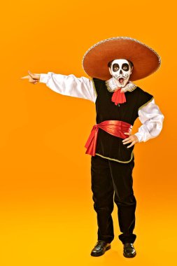 Kafatası şekeri makyajlı heyecanlı duygusal çocuk portresi şaşırmış bir parmağı işaret ediyor. Parlak sarı arka plan. Cadılar Bayramı. Dia de los muertos. Ölüler Günü.