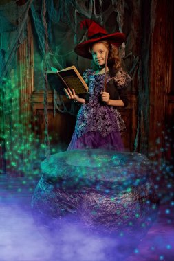 Cadılar Bayramı süslemeleri ile eski bir evde poz veren cadı kostümlü şirin mutlu kız çocuğu. Cadılar Bayramı partisi.