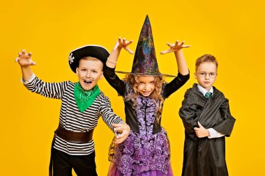 Cadılar Bayramı 'nda şeker mi şaka mı? Cadılar Bayramı kostümlü üç neşeli çocuk stüdyoda sarı bir arka planda duygusal poz veriyor. Boşluğu kopyala. 
