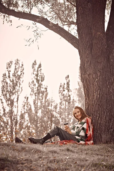 Happy beautiful girl having a rest next to the tree in an autumn park. Autumn fashion. Happiness.