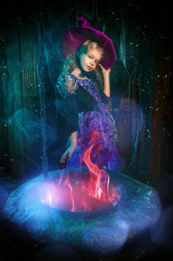 Yanan kazanda poz veren cadı kostümlü şirin mutlu kız çocuğu. Eski bir evde. Cadılar Bayramı partisi.