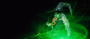 Sihirli yeşil ışıkla çevrili zehirli yılanını tutan korkunç bir cadılar bayramı cadısının portresi. Uzayı kopyala Korkunç hikayeler.. 