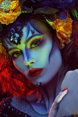 Calavera Catrina 'nın yakın plan portresi. Sarı ve kırmızı ışıkta renkli kafatası makyajlı genç bir kadın. Dia de los muertos. Ölüler Günü. Cadılar Bayramı.