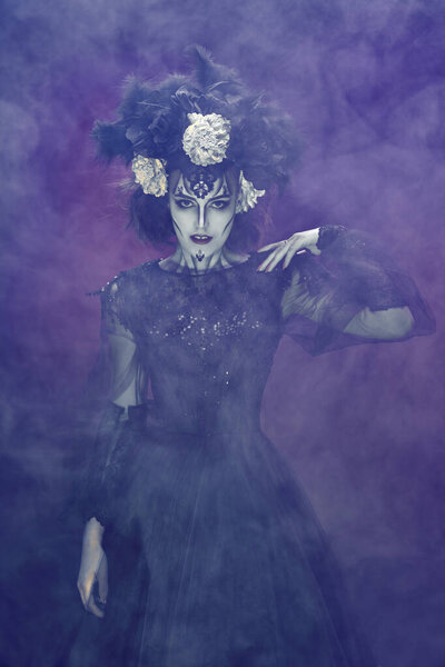 Portrait of a beautiful and scary Calavera Catrina surrounded by a mysterious fog on smoky dark background. Sugar skull makeup and costume. Dia de los muertos. Day of The Dead. Halloween.