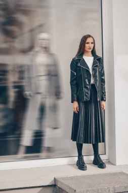 Siyah elbiseli şık bir bayan, şehir caddesinde bir moda mağazasının arka planında poz veriyor..