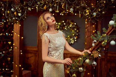 Noel ve yeni yıl büyüsü. Şenlikli bir gece elbisesi içinde, güzel bir gece makyajı ve güzel bir Noel perisi gibi saçı olan büyüleyici, mutlu genç bir kadın. Işıklar yansın.