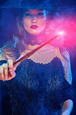 Cadılar Bayramı büyüsü. Büyülü bir değnekle genç ve muhteşem bir cadının portresi. Cadılar Bayramı partisi, makyaj ve kostüm..