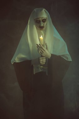 Korkunç şeytani, elinde mumla karanlık bir odada duman içinde duran bir rahibe. Korku ve Cadılar Bayramı.