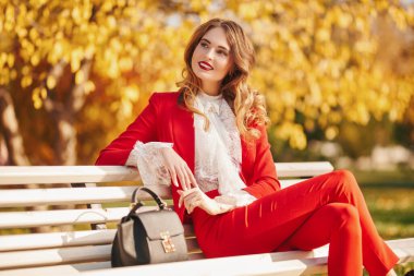 Güzel bir sonbahar parkındaki bankta dinlenen büyüleyici genç bir kadın. Güzellik, moda.