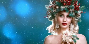 Noel kışı güzeli kadın. Kafasında Noel süsü olan çekici sarışın kız bir hediye kutusu tutuyor ve gülümsüyor. Stüdyo portresi yeşil arka planda. Boşluğu kopyala.