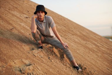 Çölde poz veren günlük yaz kıyafetleri ve panama şapkalı genç bir adamın tam boy portresi. Moda fotoğrafı.. 