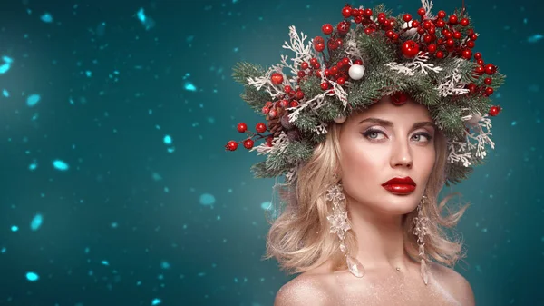 Christmas winter beauty girl. Beautiful happy young woman with a Christmas pine wreath on her head, decorated with Christmas balls, berries and snowflakes. Studio portrait over xmas green background. Copy space.