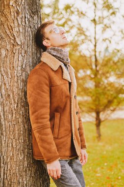 Sonbahar parkında yürüyen gözlüklü ve ceketli zarif yakışıklı bir adamın portresi. Mevsimlik güzellik, erkek modası.. 