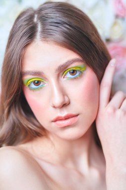 Bahar ve yaz güzelliği. Uzun dalgalı saçlı ve arkaplanda renkli makyajlı narin bir genç kadının portresi. Makyaj ve kozmetik.