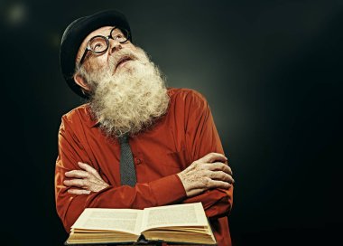 Uzun gri sakallı zeki yaşlı bir adam eski bir kitabı okuyor ve bir içgörü işareti olarak kafasını kaldırıyor. Yaşlılık bilgeliği. Yaşlı bir bilim adamı büyük bir keşif yaptı..