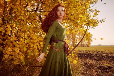 Orta Çağ 'ın güzel kızıl saçlı okçusu sonbahar ormanının yanında duruyor. Kelt kültürü. Hayal dünyası..