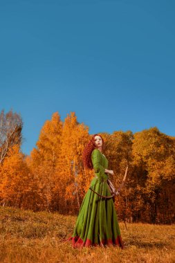 Hayal dünyası. Orta Çağ 'ın güzel kızıl saçlı okçusunun tam boy portresi bir çayırda duruyor. Kelt kültürü. Sonbahar doğası.