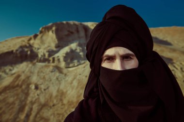 Siyah elbiseli ve başında siyah keffiyeh olan cesur genç bir adam çölde dikiliyor ve dalgın dalgın bakıyor. Maceralar, özgürlük ruhu.. 