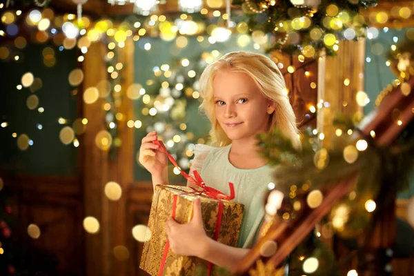 Magic for Christmas. Dreams come true. Cute little girl holds a gift box standing in a house beautifully decorated for Christmas. Happy New Year!
