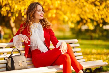 Güzel bir sonbahar parkındaki bankta dinlenen büyüleyici genç bir kadın. Güzellik, moda.