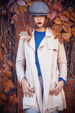 Şapkalı ve ceketli modern bir kız sonbahar çitinde duruyor. Hippi kız. Moda modeli, sonbahar tarzı..