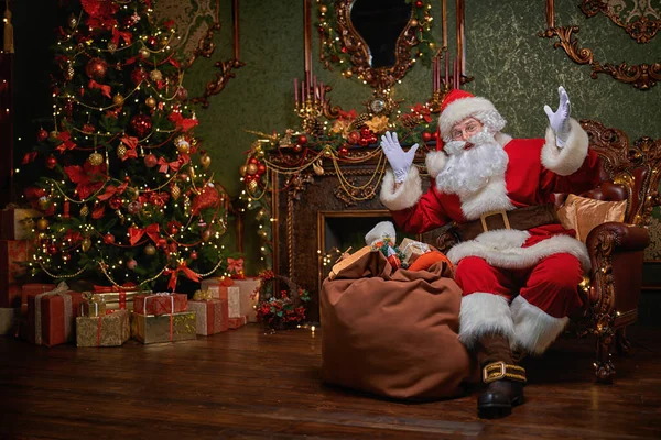 Santa Claus brought gifts for Christmas. He sits in an armchair in a beautiful Christmas interior. Christmas and New Year concept.