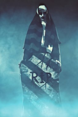 Cadılar Bayramı ve Korku. Mezarlıkta elinde bir mezar taşıyla şeytani bir rahibe. Etrafta gizemli bir sis var..