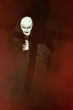 Korkunç şeytani ele geçirilmiş bir rahibe ellerinde haçla karanlık bir odada diz çöküp dua ediyor. Korku ve Cadılar Bayramı.