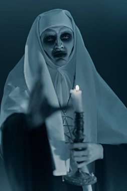 Korkunç, ele geçirilmiş bir rahibe elinde mumla karanlıkta elini uzatıyor. Korku ve Cadılar Bayramı.