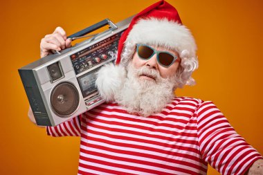 Güneş gözlüklü havalı Noel Baba 'nın elinde parlak sarı bir arka planda teyp var. Noel şarkıları ve müzik. Yeni yıl partisi.