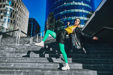 Parlak renk konsepti. Renkli kıyafetler içindeki modern kız büyük bir şehirde gökdelenlerin arkasında poz veriyor. Moda fotoğrafı..