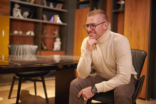 Happy middle-aged man in elegant casual clothes and glasses having a rest at home. Everyday life. Home interior concept.