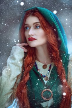 Noel Masalı. Uzun kızıl saçlı, ortaçağ kıyafetleri giyen güzel bir genç kadının portresi karlı bir ormanda yürüyor. Orta Çağ 'ın erken dönemlerinin tarihi yeniden yapılandırması.. 