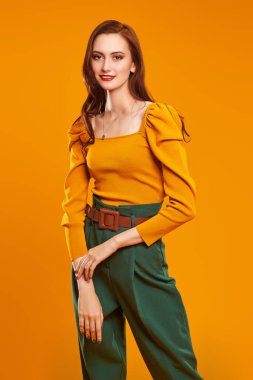 Renkli kıyafetler içinde, turuncu arka planda kameraya gülümseyen güzel, modern bir kızın portresi. Moda fotoğrafı. Giysilerdeki parlak renkler. 