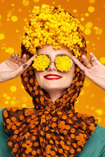 Fashion and colors. Floral concept. Portrait of a high fashion woman posing with mimosa flowers on her head and glasses. Bright saturated colors. Pin-up style.