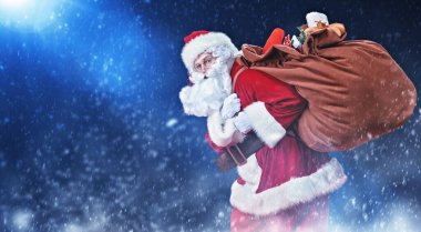 Yaşlı Noel Baba, karın altında hediyeler taşıyan büyük bir çanta taşıyor. Sihirli Noel gecesi.