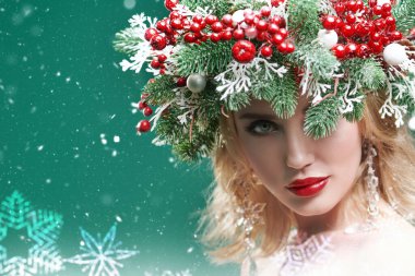 Noel kış kızı. Kafasında Noel çelengi olan, Noel topları, böğürtlen ve kar taneleriyle süslenmiş güzel bir genç kadın. Karlı yeşil arkaplan. Boşluğu kopyala.
