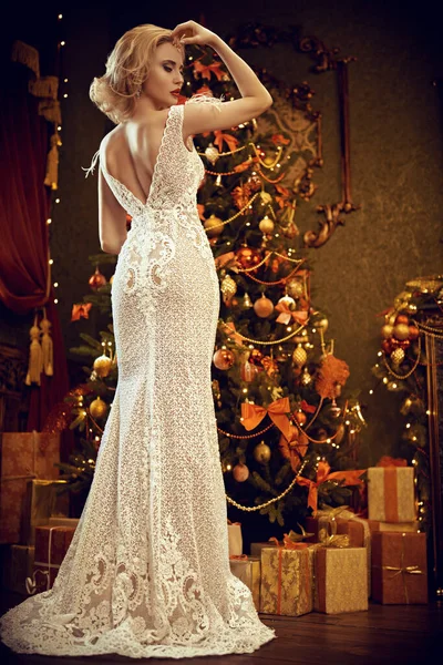 Evening fashion. Charming young woman in luxurious evening dress meets Christmas at the New Year tree.