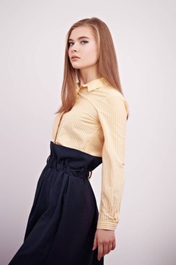 Zarif bir bluz ve beyaz bir arka planda poz veren etekli güzel bir genç kadın. İş kadını..