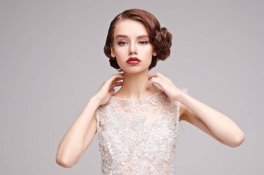 Akşam makyajı ve saç stili. Gri arka planda, lüks beyaz elbiseli çekici genç bir kadının portresi. Saç ve makyaj 20 'li yılların tarzında.. 