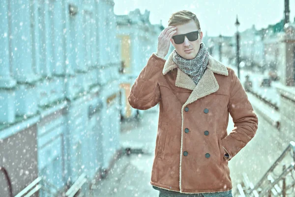 Men\'s style. Handsome young man in winter coat and scarf stands on the street in the city. Winter fashion, clothing and accessories.