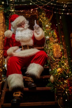 Mutlu Noeller ve mutlu yıllar! Neşeli Noel Baba, güzel bir yeni yıl arifesinde tahta bir merdivende duruyor.. 