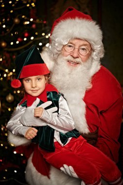 Nazik Noel Baba ve elfi evdeki koltukta dinleniyorlar. Noel ve Yeni Yıl masalları.