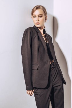 Beyaz duvarda poz veren siyah takım elbiseli güzel sarışın bir kadının portresi. Moda fotoğrafı.. 