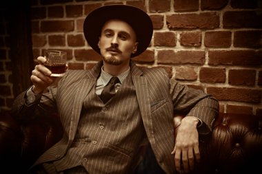 Yakışıklı sarhoş bir adam deri koltukta bir bardak viskiyle rahatça oturuyor. Lüks bir yaşam tarzı. Retro tarzı. Mafya ve suç dünyası. 