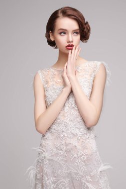 Akşam makyajı ve saç stili. Gri arka planda, lüks beyaz elbiseli çekici genç bir kadının portresi. Saç ve makyaj 20 'li yılların tarzında.. 