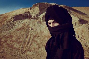 Siyah elbiseli ve başında siyah keffiyeh olan cesur genç bir adam çölde dikiliyor ve dalgın dalgın bakıyor. Maceralar, özgürlük ruhu.. 