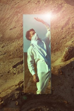 Reflection of a handsome young man in white clothes looking to the sun standing in a desert. Fashion shot.  clipart