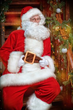 Mutlu Noeller ve mutlu yıllar! Neşeli Noel Baba, güzel bir yılbaşı gecesinde tahta bir merdivende oturur.. 